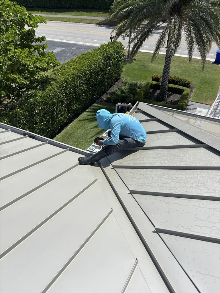 A Happy Home Detailing employee on the metal roof of a house, cleaning out the gutter.